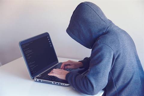 Ilustrasi peretas dalam hoodie gelap di depan layar kode